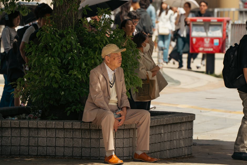 Elderly man sitting by plants in Tokyo streets, surrounded by pedestrians.