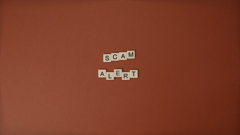 Scrabble tiles spelling Scam Alert on a brown surface indicating caution.
