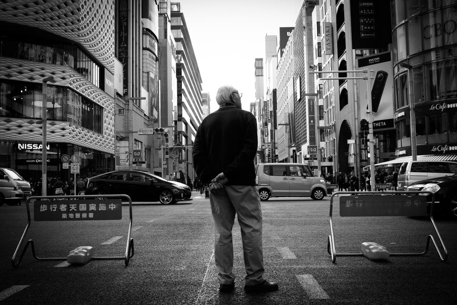 Black and white photo of an elderly man standing in a busy Tokyo street, capturing urban life.