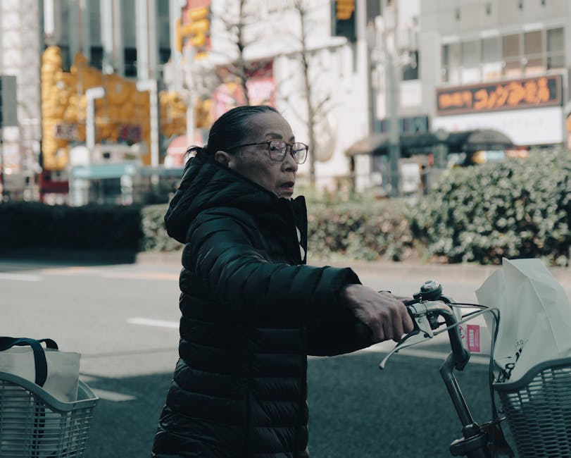 Elderly woman cycling in bustling Tokyo street, urban lifestyle scene.