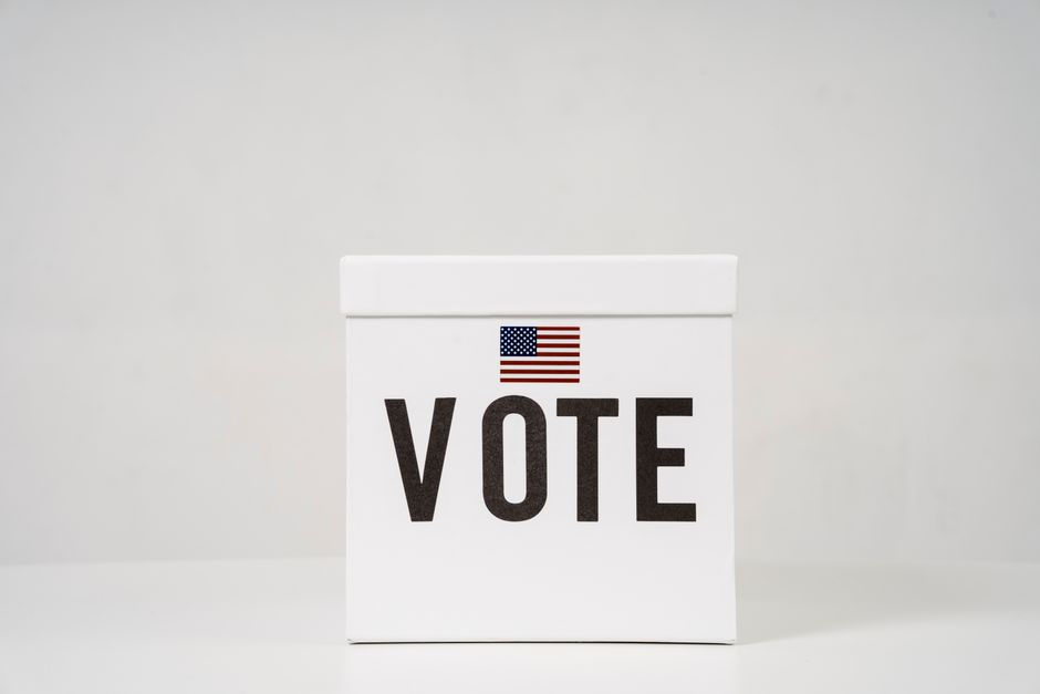 A minimalist ballot box with 'Vote' and an American flag, symbolizing elections.
