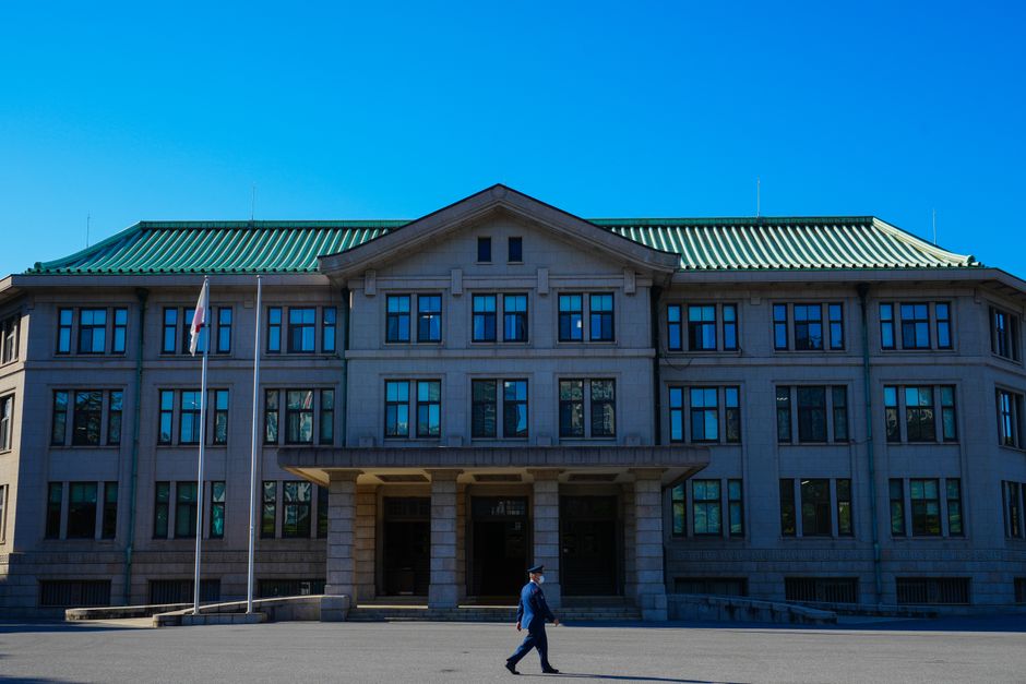 An architectural view of a government building with a person walking past under a clear blue sky.