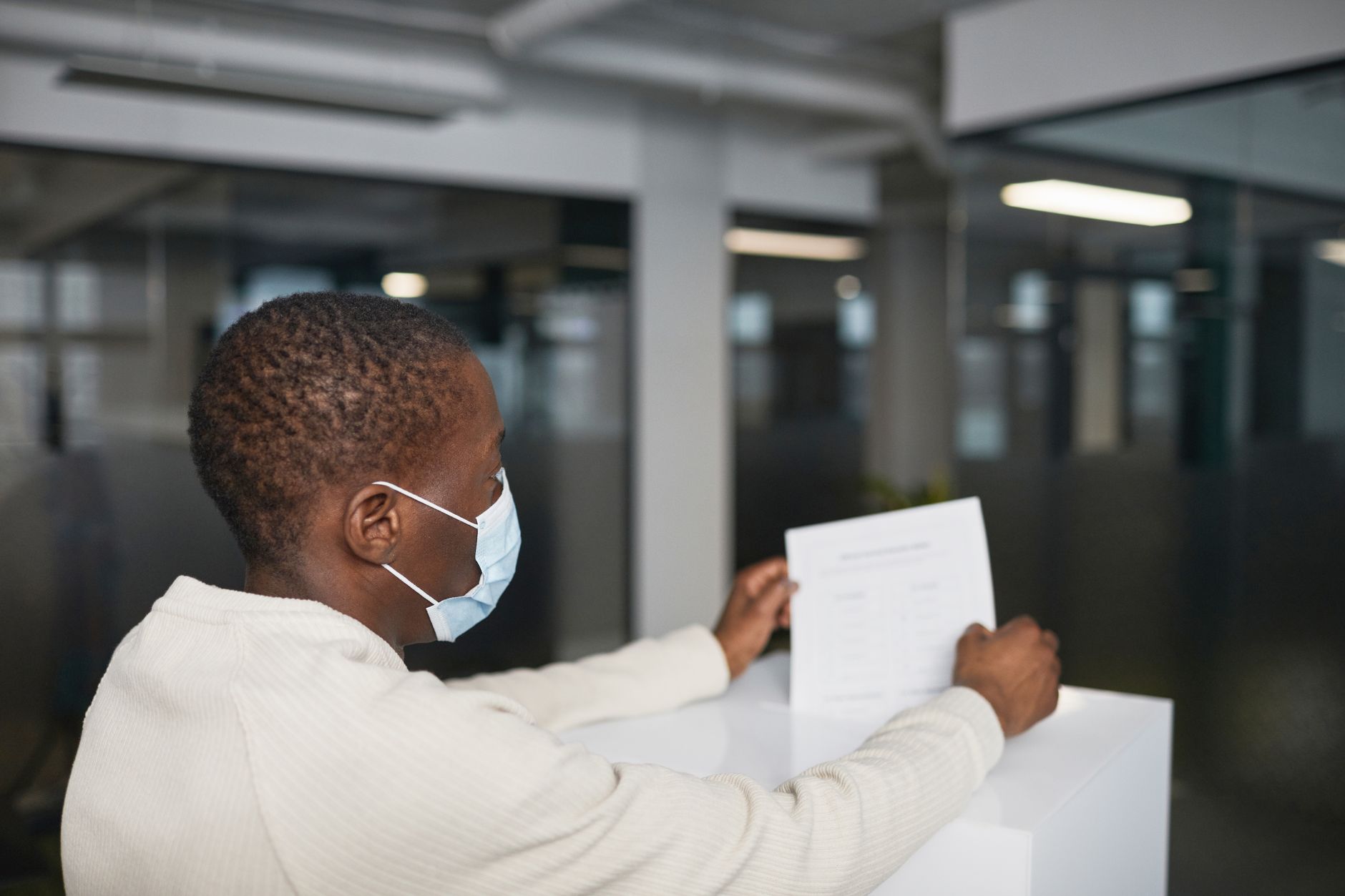 An individual wearing a face mask casts their vote in an indoor setting, representing voting during the pandemic.