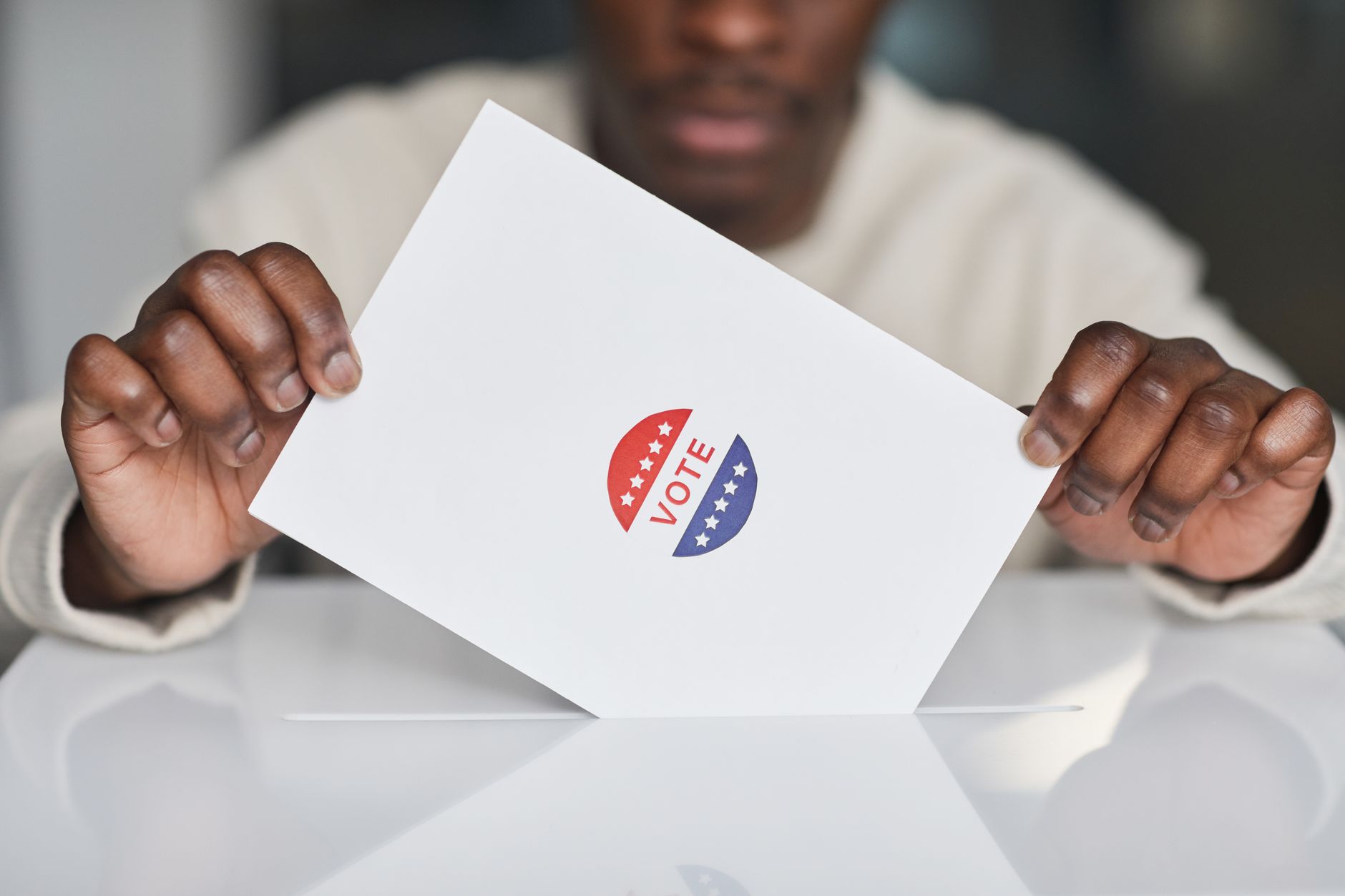 A voter placing a ballot into a box during an election. Focus on the act of voting.