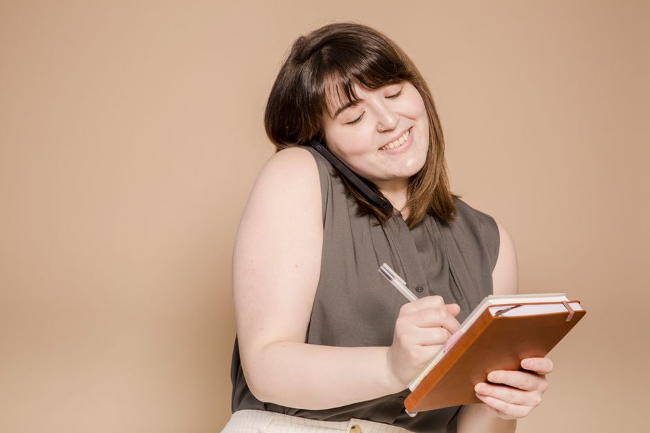 A person on a phone call taking handwritten notes on a notepad at home