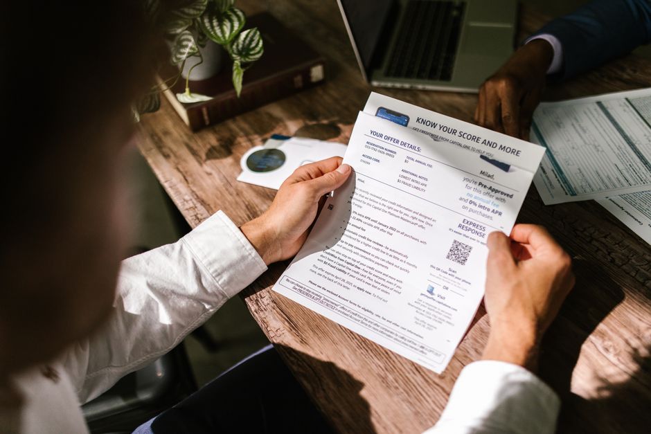 A person at a kitchen table reading a printed bank statement closely