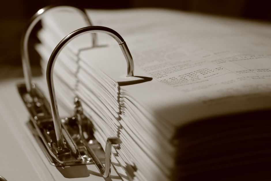 Tall stacks of thick binders and paper documents on an office table