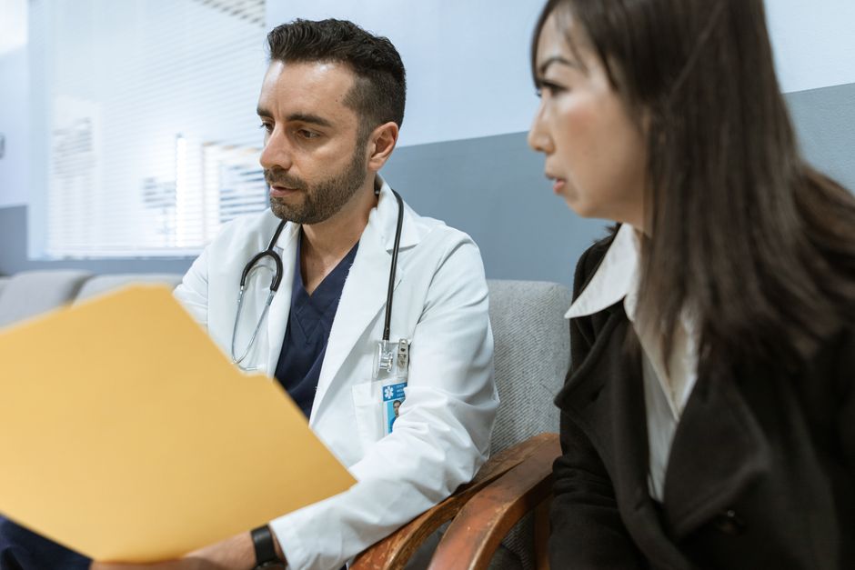 A doctor talking with a seated patient across a desk in a clinic room