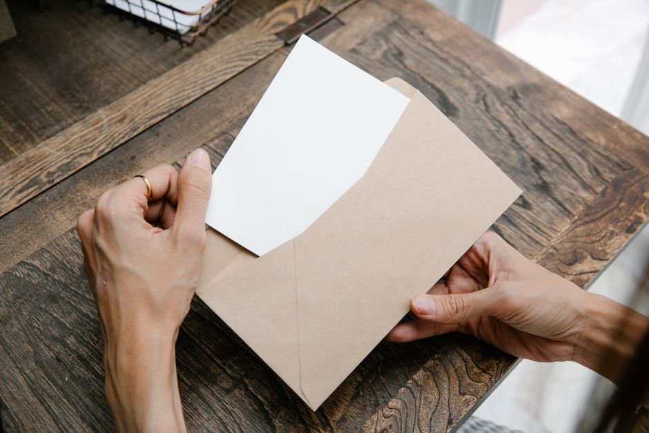 A person opening a formal printed letter at a desk with a laptop nearby