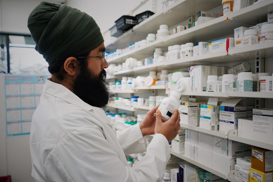 A pharmacist checking a prescription bottle in front of pharmacy shelves