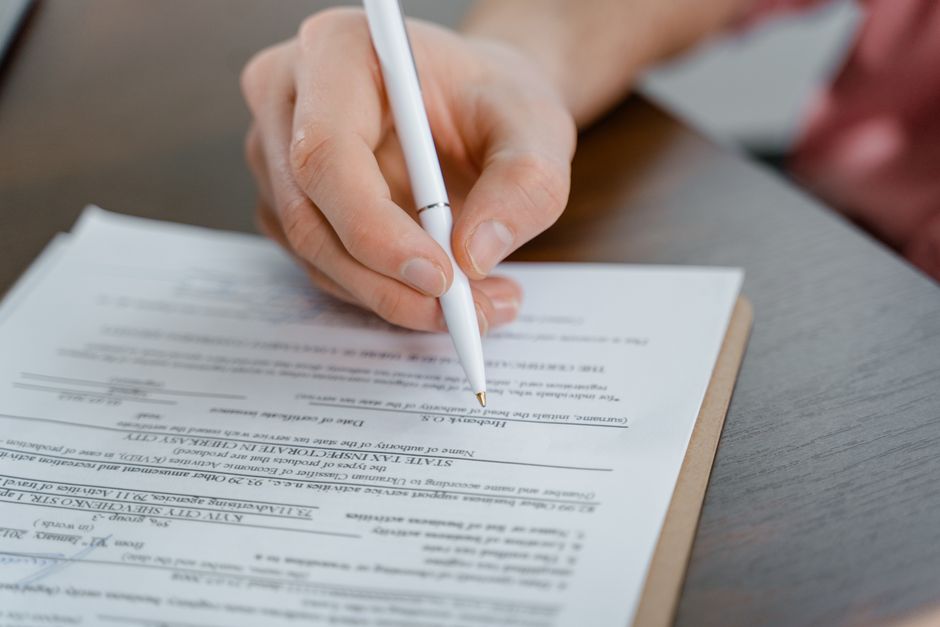 Hands filling in a printed legal claim form with a blue pen on a desk