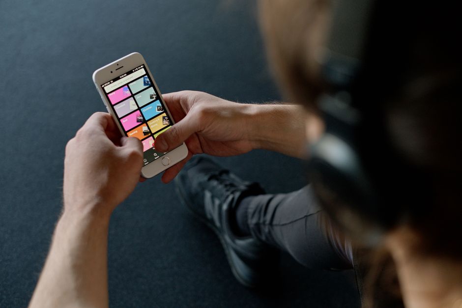 A listener scrolling a music streaming app on a smartphone with headphones nearby