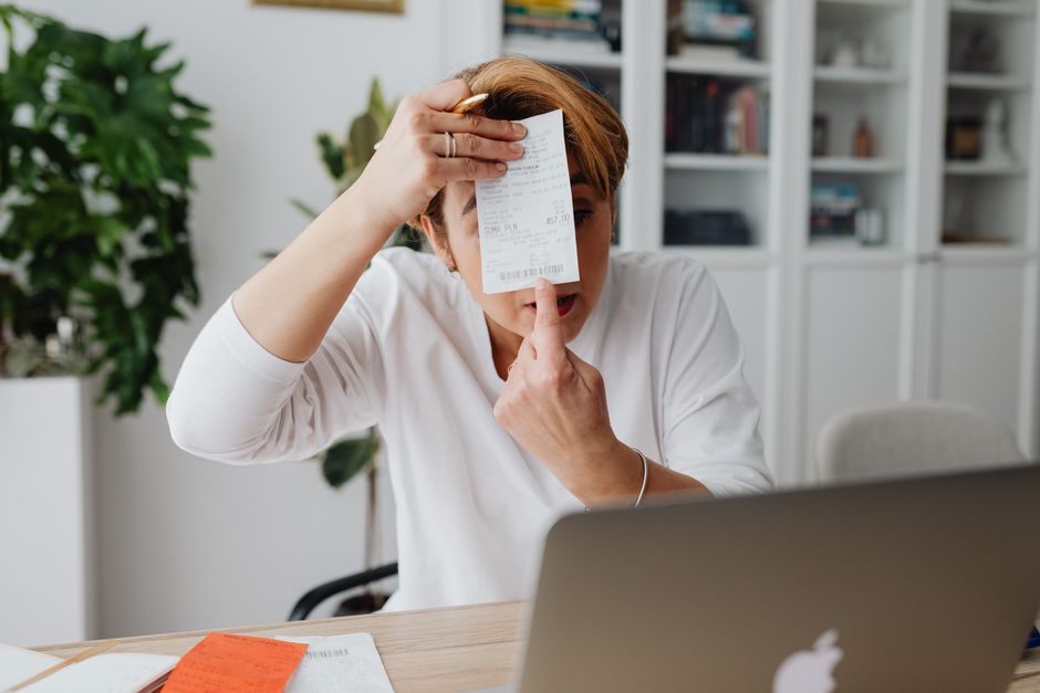 Person at a kitchen table examining a paper utility bill with a pen