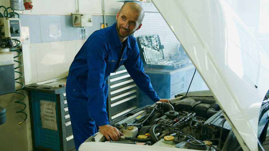 A mechanic working under the hood of a car inside an independent auto repair shop