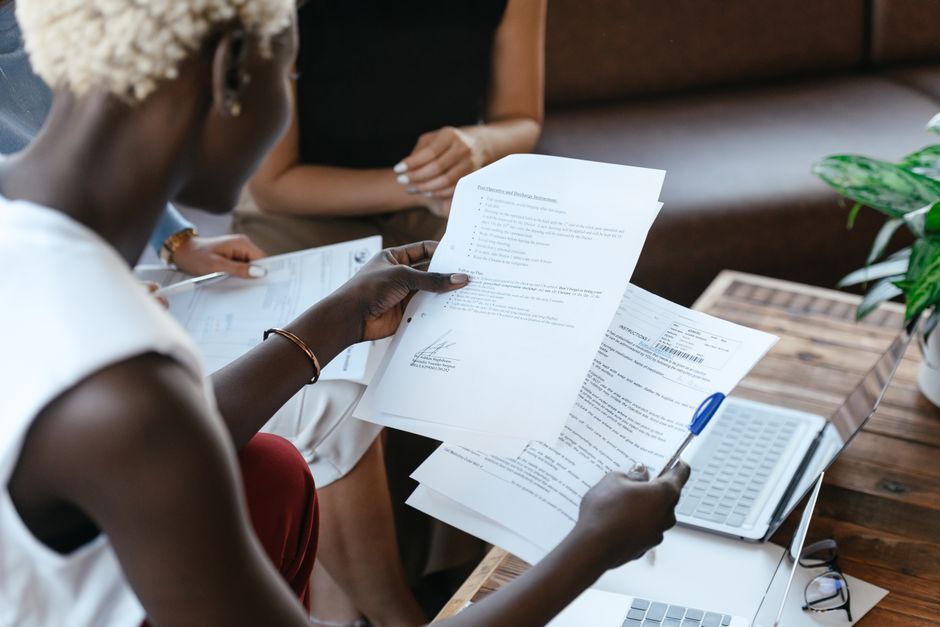 A person at a desk comparing two printed documents side by side with a pen in hand
