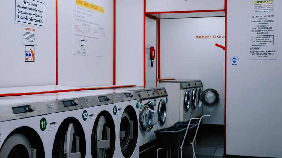 A repair technician kneeling beside an open washing machine with tools on the floor