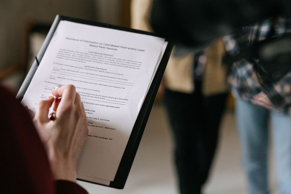 A person signing real estate closing paperwork at a desk with a pen and folder