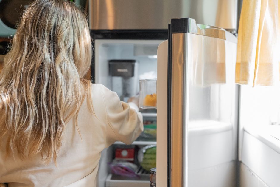 Open home refrigerator showing containers of leftovers and packaged foods on shelves