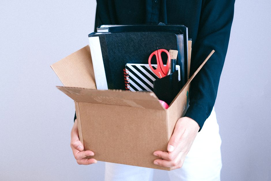 A worker carrying a cardboard box of belongings out of an office