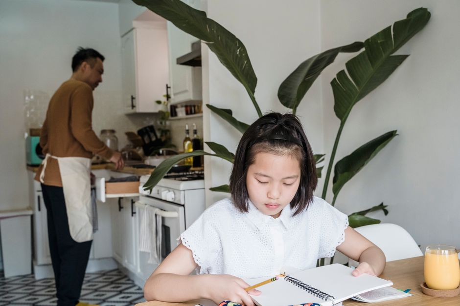A parent sitting at a kitchen table helping a young child with homework