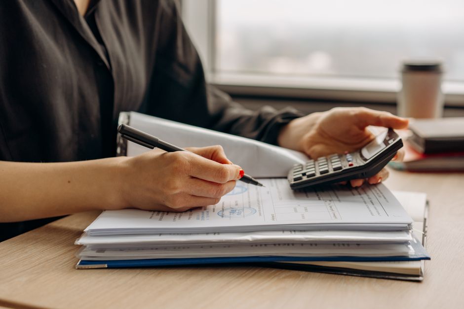 Hands using a calculator next to printed estimate paperwork on a desk