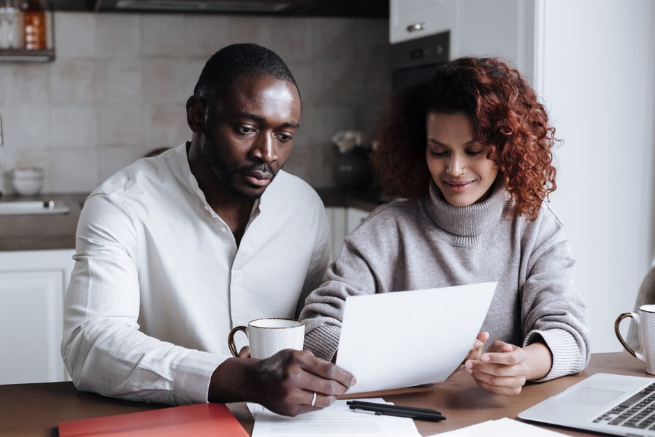 Two people at a kitchen table reading a letter and comparing printed estimates