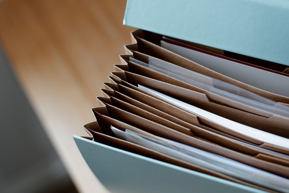 A tall stack of manila file folders and paperwork on an office desk