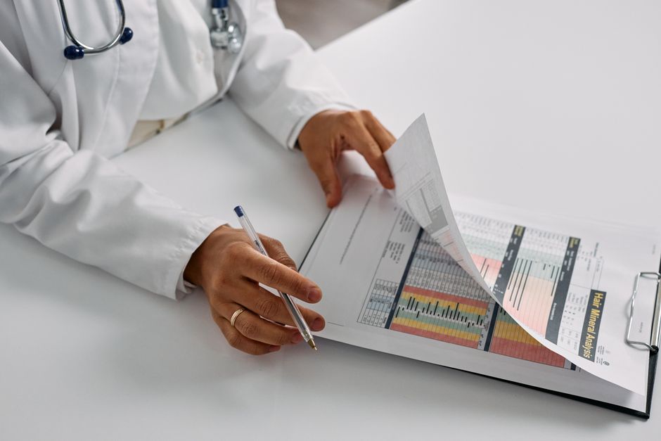 A physician in a white coat reading through a stack of printed medical records at a desk