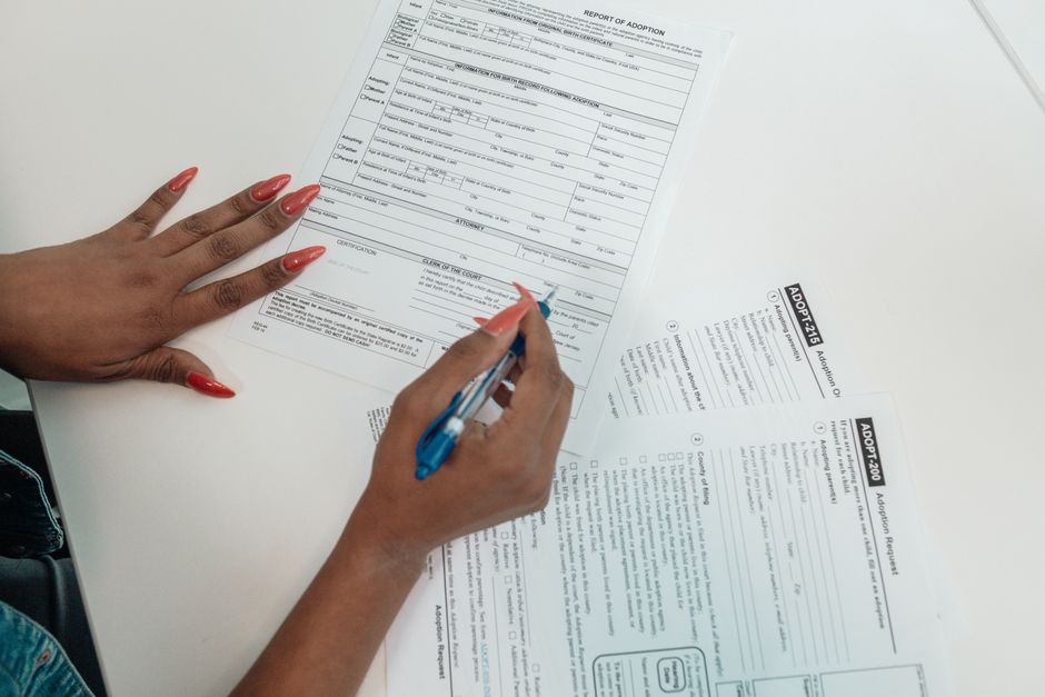 A seated person completing a paper application form with a pen on a wooden table
