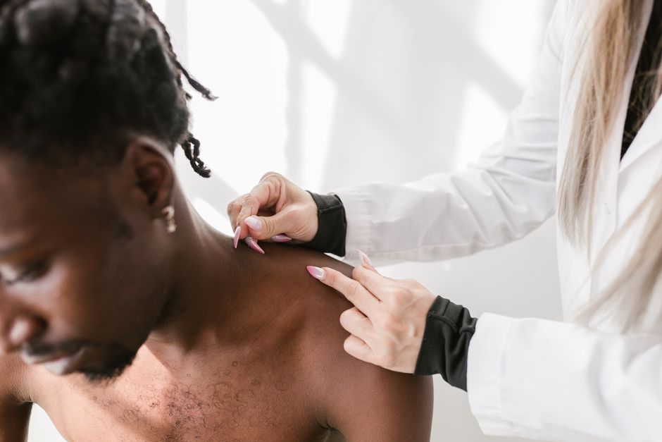 A doctor in a clinic examining a seated patient's shoulder during a follow-up visit