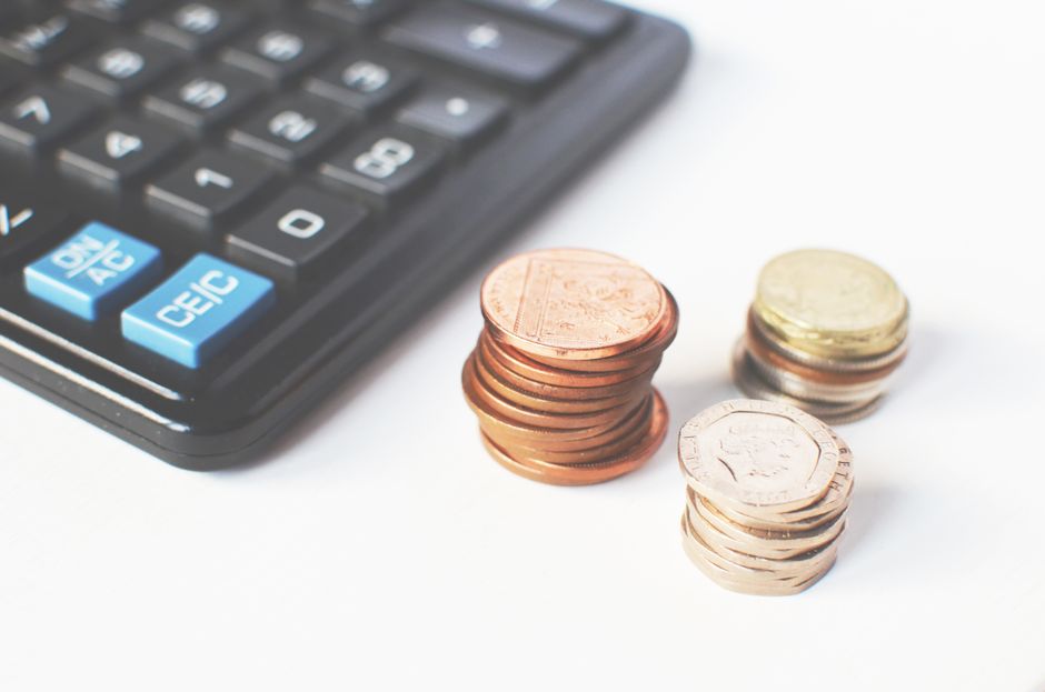 A calculator resting on printed pay stubs next to a pen on a wooden table