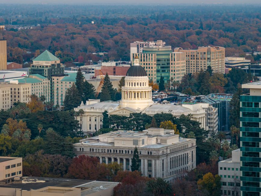 A state capitol building with a domed roof seen from the front steps